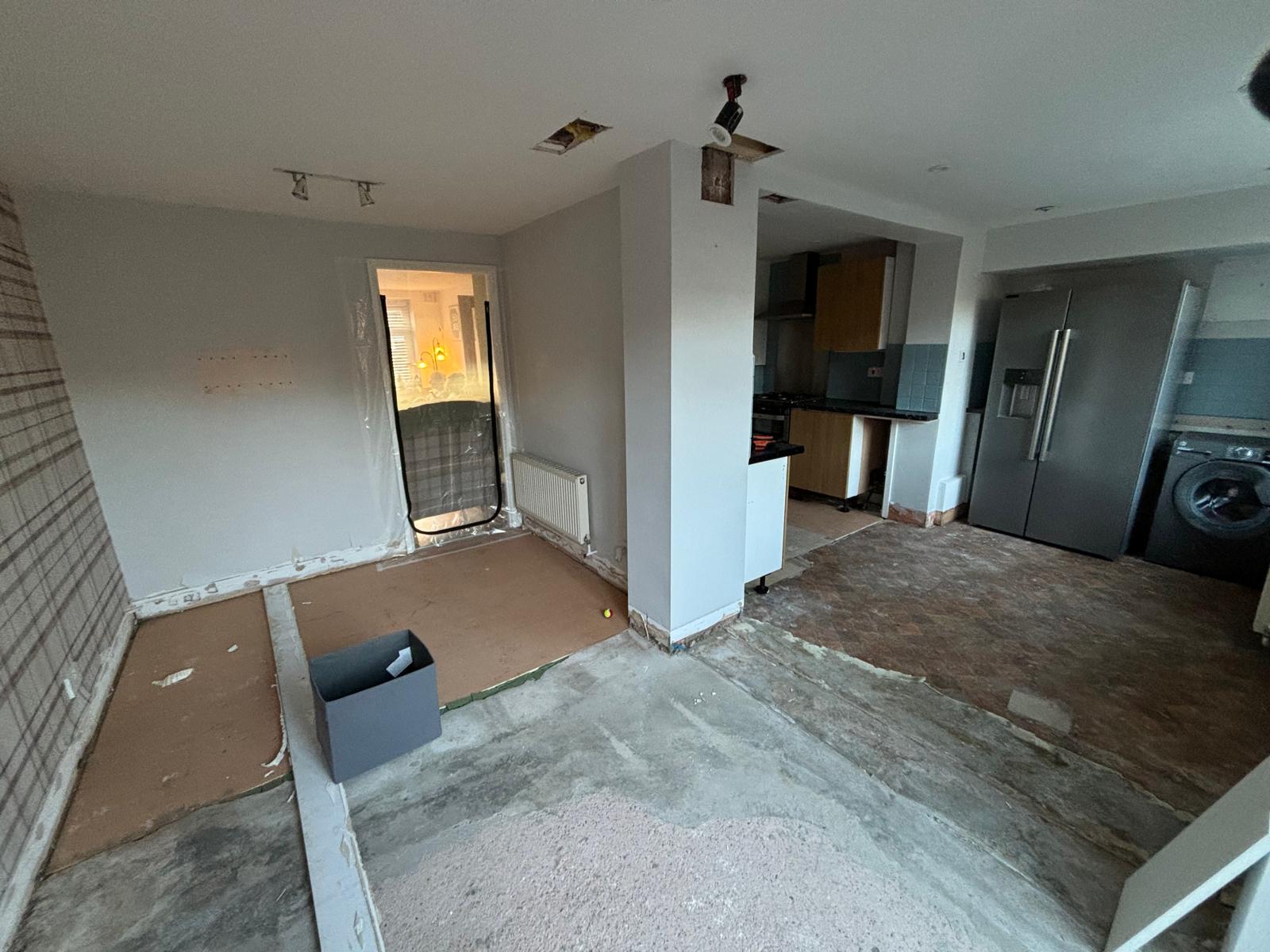 Kitchen renovation in progress with stripped flooring, exposed walls, and partially removed units